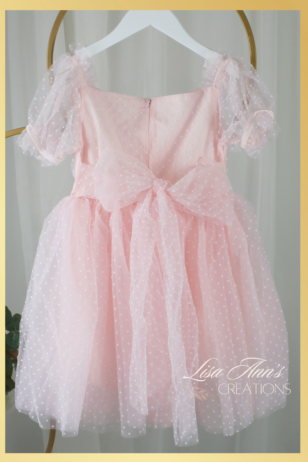 back of dress with a big bow. dress is a swiss dot pattern in light pink with puff short sleeves and knee length style.